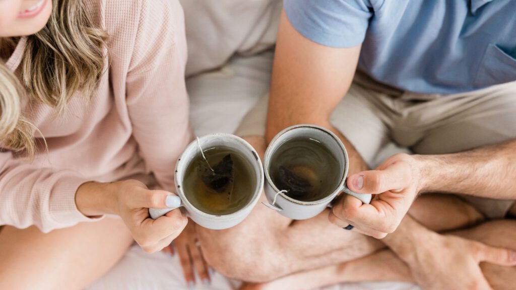Um casal sentado brindando o momento, com canecas de chá.