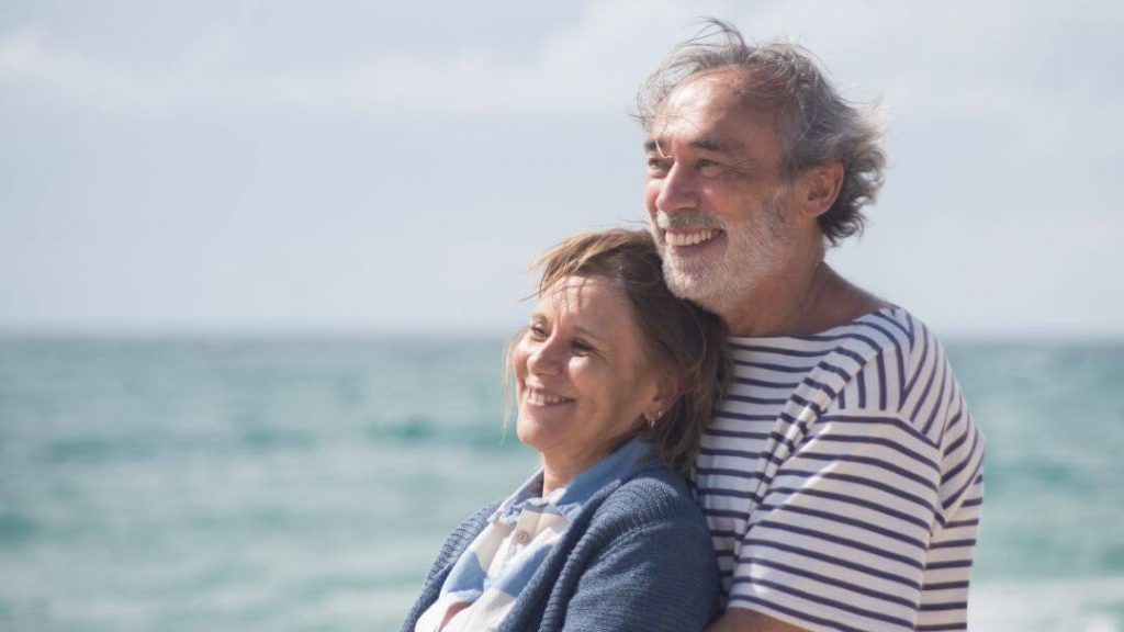 Casal de idosos, vivendo a envelhescência, sorrindo olhando para o horizonte na praia.