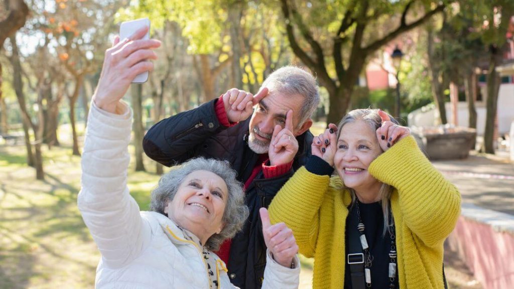 Grupo de três idosos posando para uma foto self fazendo careta. 