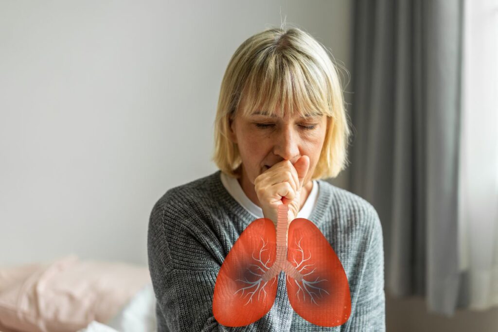 Mulher adulta, por volta dos 50 anos, branca, está tossindo. Na frente do peito dela há uma ilustração do pulmão. A foto ilustra os problemas respiratórios da DPOC que podem se agrava no outono, enfisema e bronquite crônica.