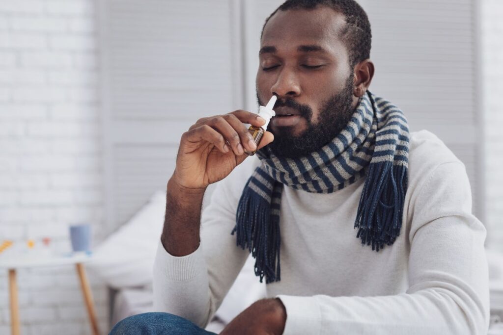 Homem jovem negro fazendo uso de descongestionante nasal.